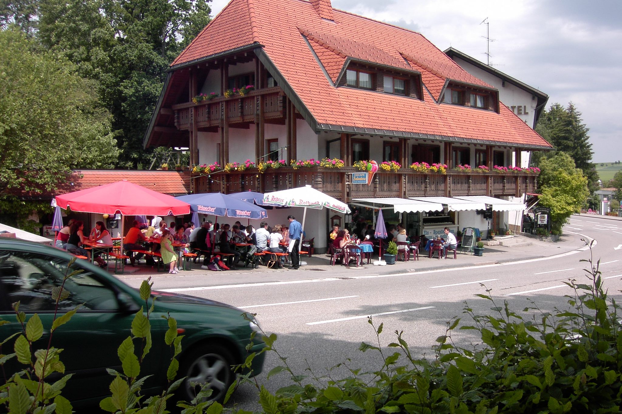 Älteres Gebäude mit großem Ziegeldach, Gäste auf der Terrasse mit Sonnenschirm. Eiscafe Salvatore in Bonndorf.
